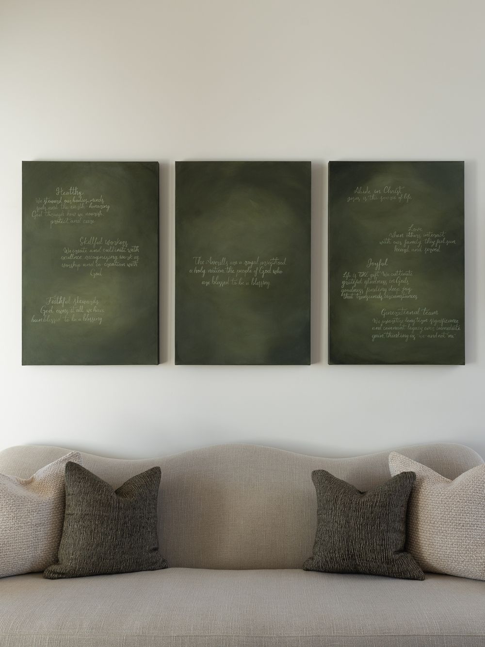 Three hand-lettered deep-green canvases hanging above a linen sofa, holding a family's written values